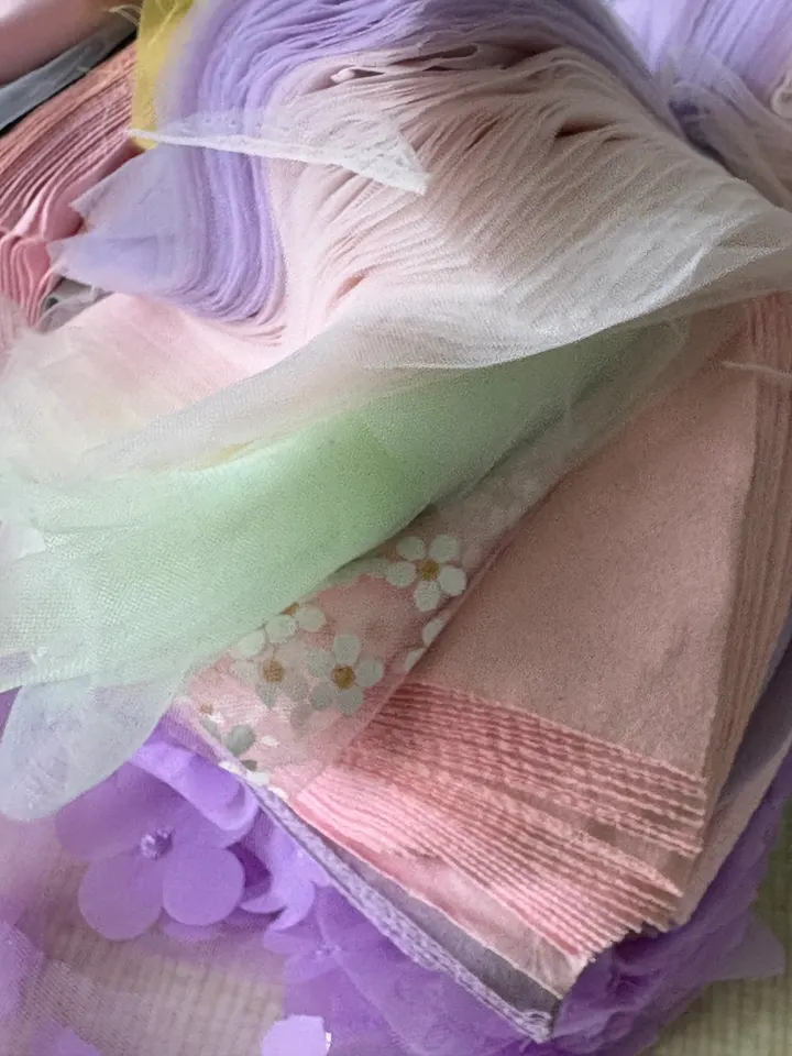 Een stapel pastelkleurige stoffen: tule, geplisseerd roze en lila met opgestikte bloemen