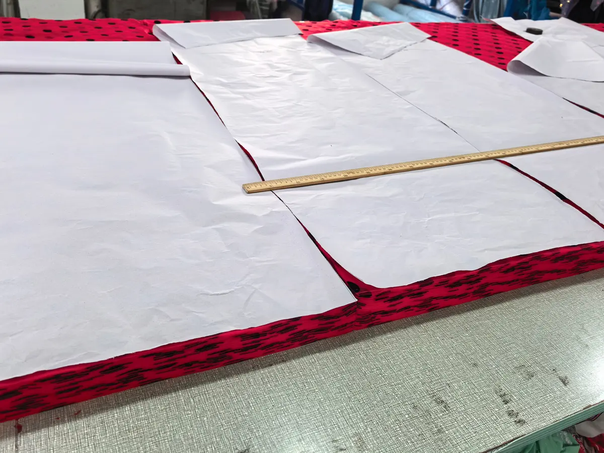 Papieren patroondelen met een houten meetlat op rode stof met zwarte stippen