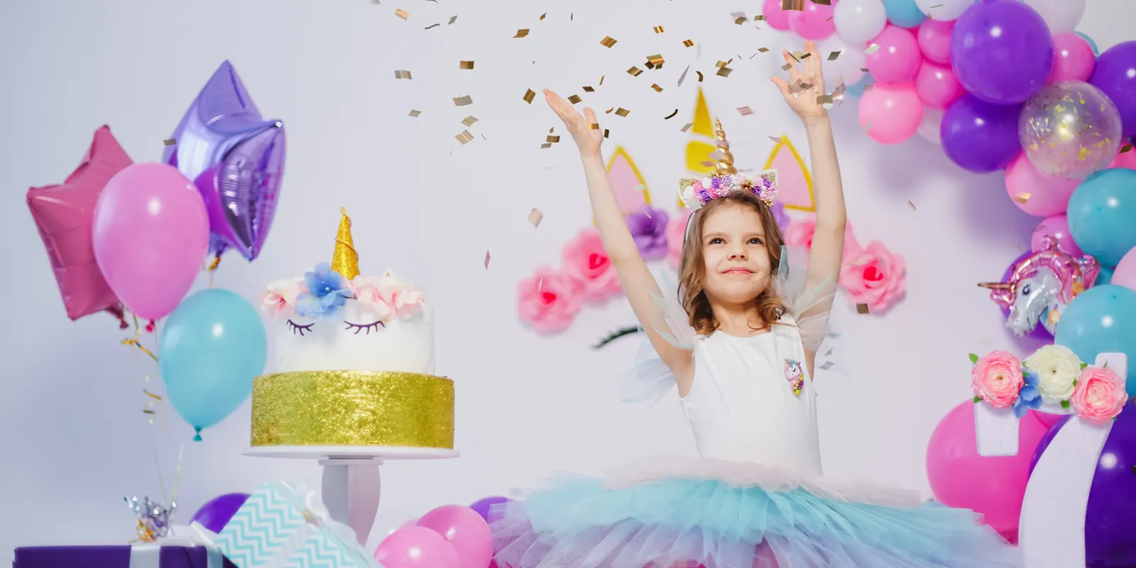 Meisje in een tutu met eenhoorn-haarband tussen ballonnen, met een taart en confetti